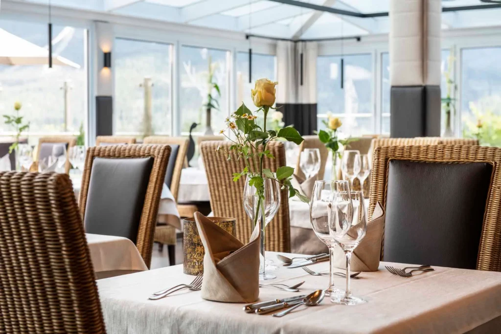 Eleganter Restauranttisch im Hotel Hubertushof mit gelber Rose, Gläsern und Besteck im hellen Wintergarten.