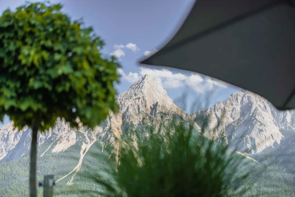Blick von der Terrasse des Hotel Hubertushof unter einem Sonnenschirm auf die imposanten Tiroler Berggipfel.