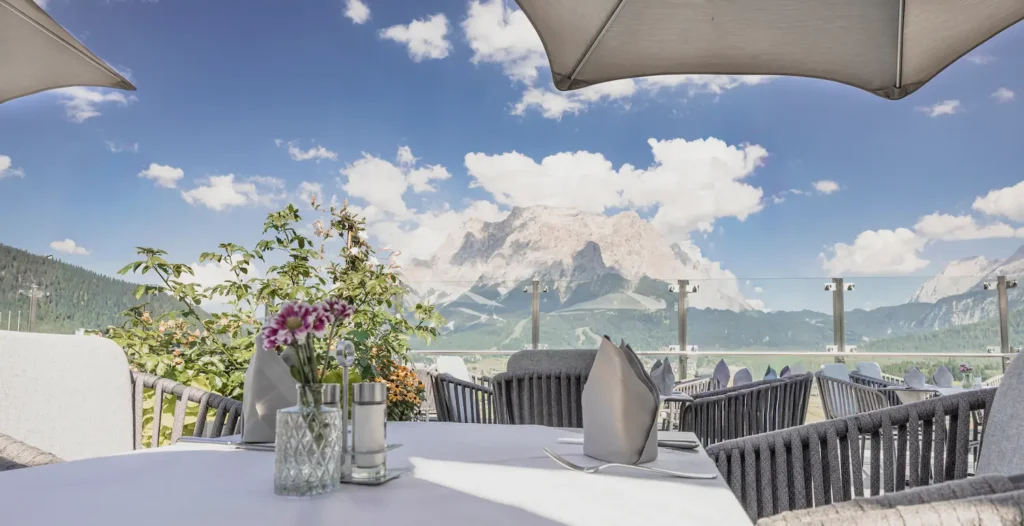 Deckter Tisch auf der Sonnenterrasse des Hotel Hubertushof mit Sonnenschirm und spektakulärem Blick auf die Berge.