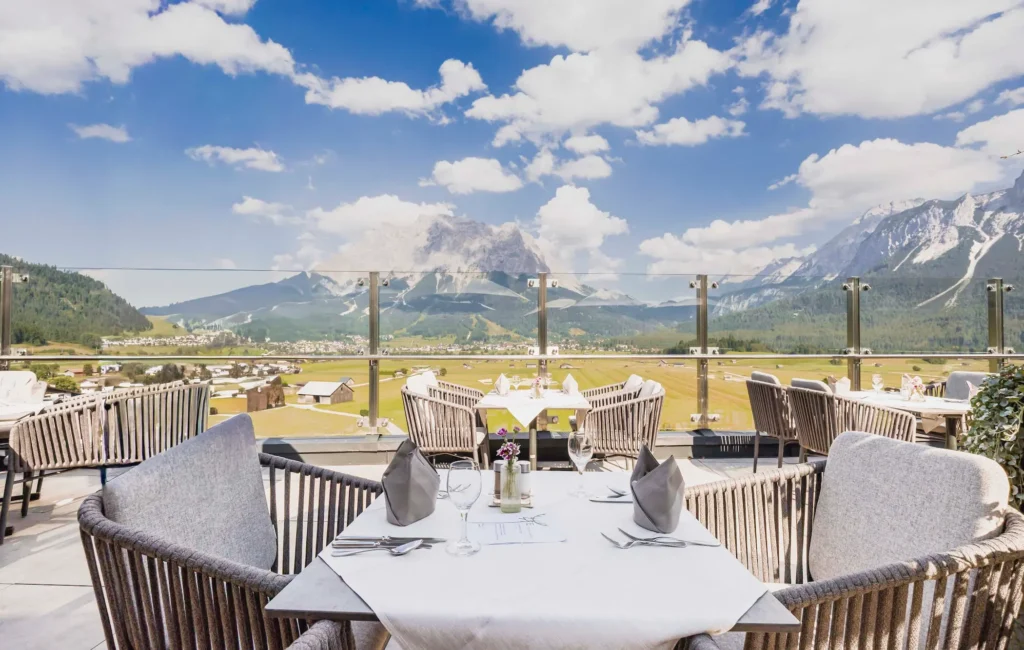 Eingedeckte Tische auf der Sonnenterrasse des Hotel Hubertushof mit freiem Blick auf das Tal und die Alpen.